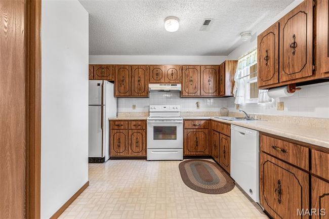 Kitchen featuring white appliances, under cabinet range hood, brown cabinets, and a textured ceiling | Image 17