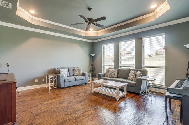 Living area with ceiling fan, visible vents, wood finished floors, a raised ceiling, and baseboards | Image 21