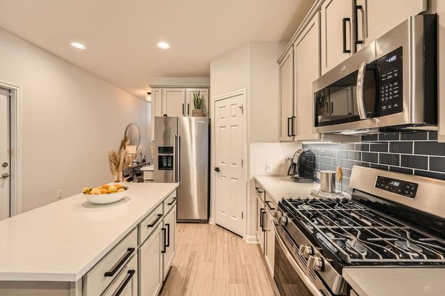 Kitchen featuring light wood finished floors, decorative backsplash, light countertops, and stainless steel appliances | Image 13