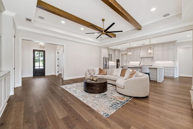 Living area featuring dark wood finished floors, ornamental molding, a ceiling fan, beamed ceiling, and a raised ceiling | Image 12