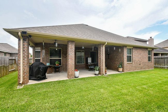 Backyard with a covered patio attached to a brick house. The patio features seating, potted plants, and a grill, all set against a well-maintained lawn and fenced yard, offering a comfortable outdoor living space. | Image 29