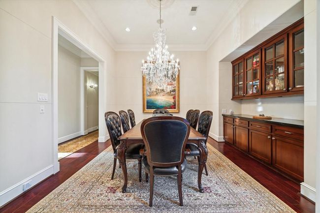 This elegant dining room features a luxurious chandelier and a built-in glass cabinet. The area is accented with a large rug and tasteful artwork, creating a warm and sophisticated atmosphere. | Image 9
