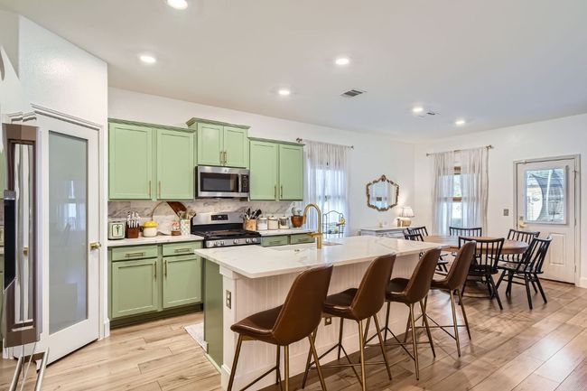 Kitchen featuring appliances with stainless steel finishes, green cabinetry, a breakfast bar area, a center island with sink, and decorative backsplash | Image 11
