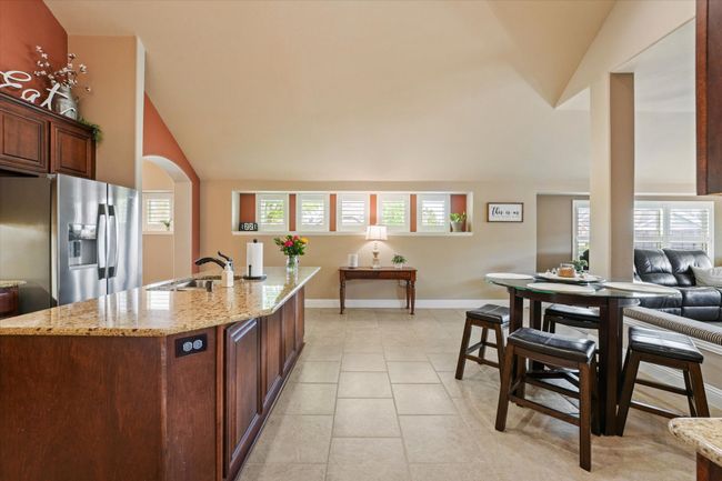 Kitchen featuring vaulted ceiling, a sink, stainless steel fridge, baseboards, and light stone countertops | Image 12
