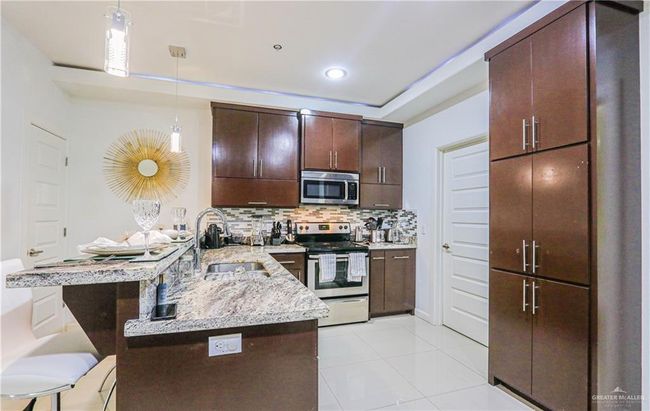Kitchen featuring kitchen peninsula, dark brown cabinetry, stainless steel appliances, sink, and hanging light fixtures | Image 10