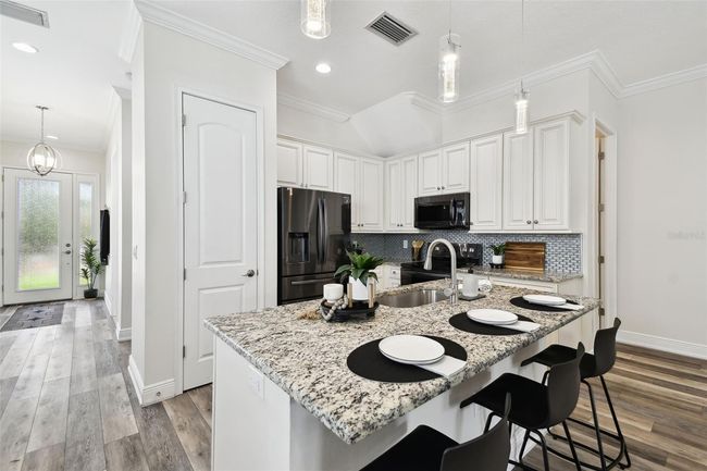 Spacious kitchen with 42" cabinets, granite tops, black stainless appliances, granite, tile backsplash, and custom pendant lighting. | Image 6