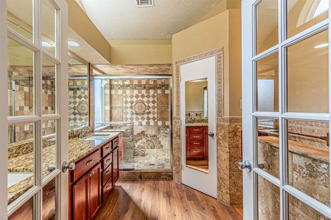 Full bath featuring double vanity, wood finished floors, a shower stall, a textured ceiling, and tile walls | Image 18
