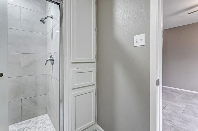 A closer look at the shower reveals stylish, oversized tiles and a polished chrome showerhead, adding a spa-like feel. Built-in shelving and soft lighting complete this updated bathroom, offering a luxurious and practical retreat. | Image 19