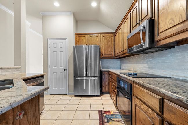 Kitchen featuring black appliances, backsplash, light stone countertops, light tile patterned floors, and vaulted ceiling | Image 14
