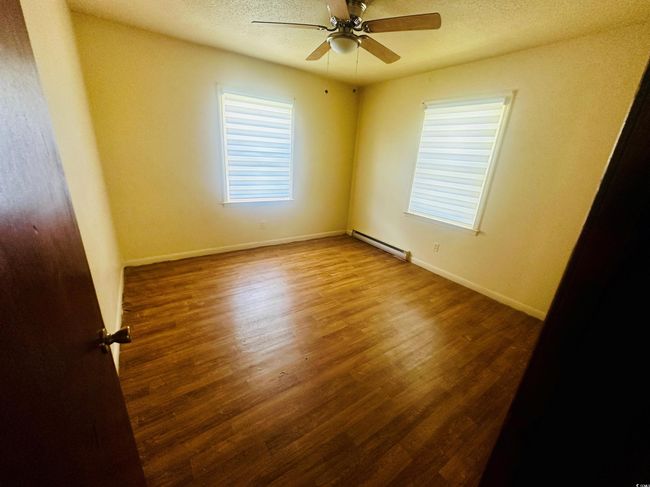 Unfurnished room featuring baseboard heating, wood finished floors, ceiling fan, a textured ceiling, and baseboards | Image 16