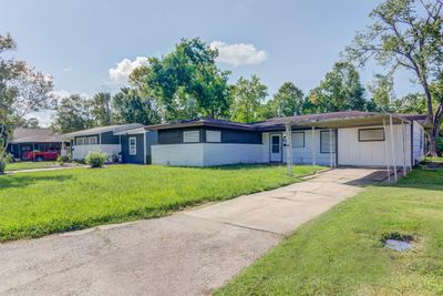 This is a single-story home featuring a low-pitched roof and an attached carport. The exterior has shutters on the windows and a concrete driveway. | Image 2