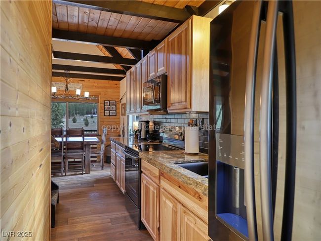 Kitchen with beam ceiling, a chandelier, wood walls, dark wood-type flooring, and black appliances | Image 13