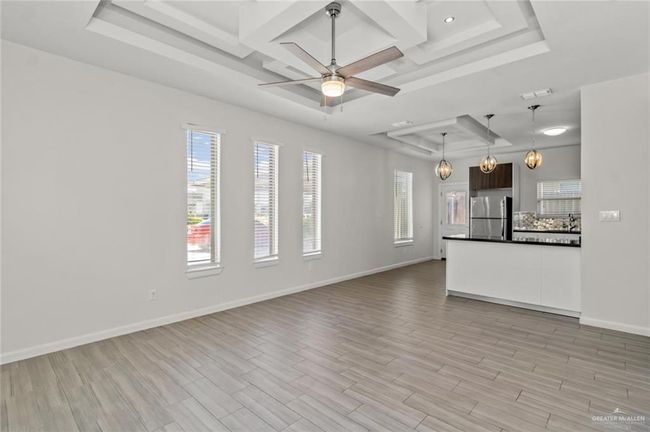 Unfurnished living room featuring a tray ceiling, coffered ceiling, light wood finished floors, ceiling fan, and beamed ceiling | Image 4