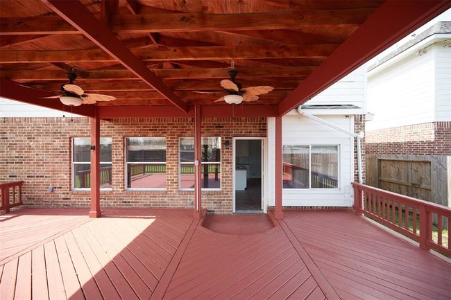 This photo showcases a spacious, covered wooden deck with ceiling fans, perfect for outdoor entertaining. It is attached to a brick house, featuring large windows and a door leading inside, with a fenced yard providing privacy. | Image 47