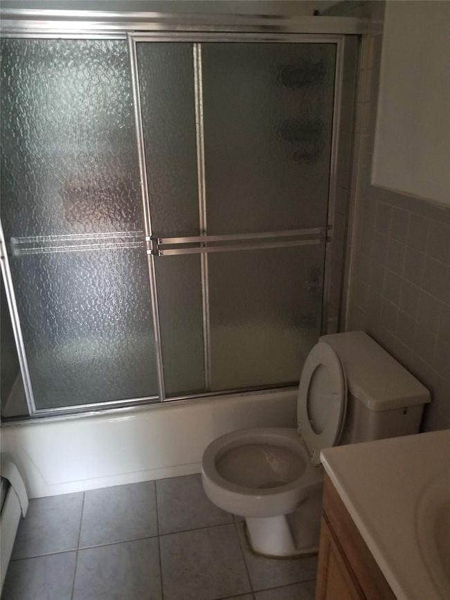 Full bathroom featuring vanity, toilet, tile walls, tile patterned flooring, and bath / shower combo with glass door | Image 7