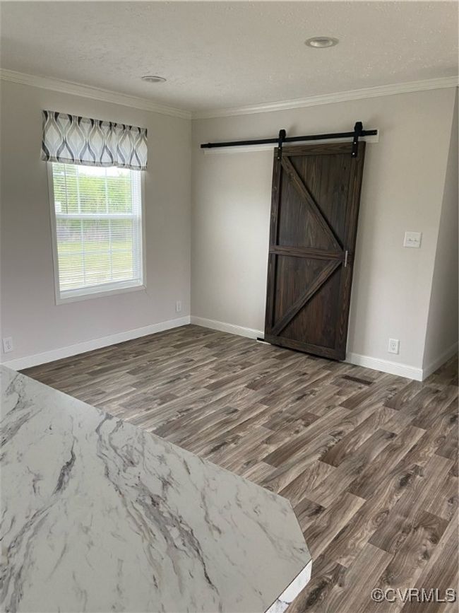 Unfurnished room with wood-type flooring, ornamental molding, and a barn door | Image 8