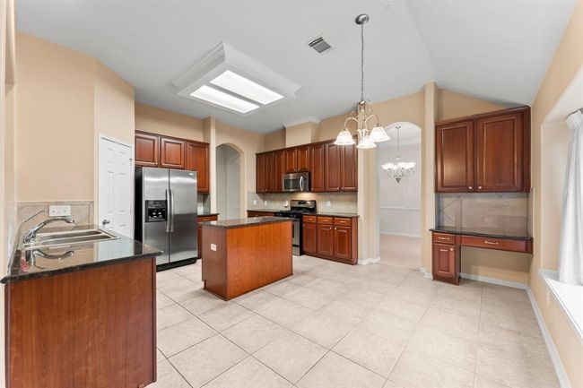 This well-appointed kitchen features rich wood cabinetry, granite countertops, stainless steel appliances, and a central island ideal for meal prep or casual dining. With an open layout, built-in desk, and easy access to the dining room, it's designed for both functionality and effortless entertaining. | Image 8