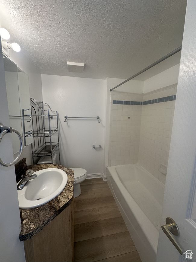 Full bathroom with vanity, a textured ceiling, wood finished floors, and washtub / shower combination | Image 4