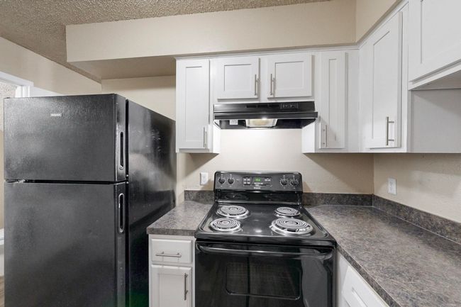 Kitchen with under cabinet range hood, dark countertops, black appliances, and white cabinetry | Image 21