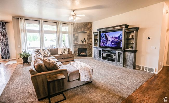 Living area with wood finished floors, a ceiling fan, a stone fireplace, and baseboards | Image 15