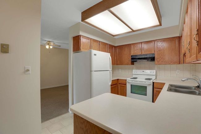 Kitchen with white appliances, under cabinet range hood, backsplash, and brown cabinets | Image 13