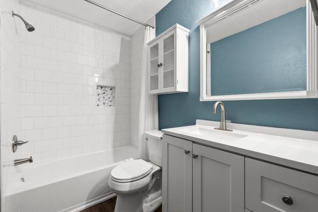 Bathroom featuring shower / bath combination with curtain, vanity, toilet, wood finished floors, and a textured wall | Image 14