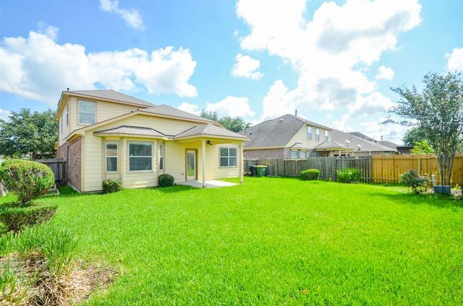This photo shows a spacious backyard with lush green grass and a well-maintained two-story house featuring light-colored siding and multiple windows, offering a bright and inviting outdoor space. | Image 32