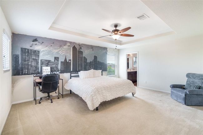 Retreat to the luxurious primary bedroom, a true sanctuary featuring plush carpet, sophisticated trey ceilings, and multiple windows with privacy blinds that fill the space with soft, natural light—perfect for relaxing at the end of the day. | Image 9