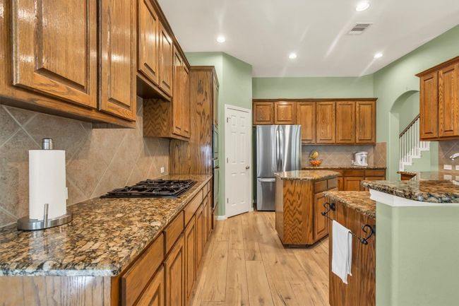 Kitchen featuring light wood finished floors, black gas cooktop, visible vents, freestanding refrigerator, and brown cabinetry | Image 14