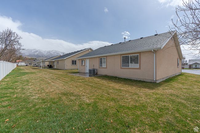 Rear view of house with a patio area, central air condition unit, fence, a lawn, and a mountain view | Image 29