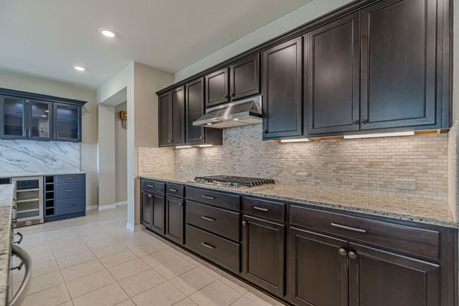 Kitchen featuring backsplash, light tile patterned flooring, beverage cooler, light stone countertops, and under cabinet range hood | Image 16