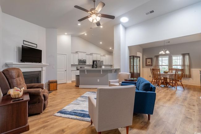 Living area with visible vents, a wainscoted wall, ceiling fan with notable chandelier, light wood-style flooring, and a glass covered fireplace | Image 19