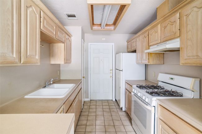 Kitchen with white appliances, under cabinet range hood, light brown cabinetry, a sink, and light countertops | Image 9