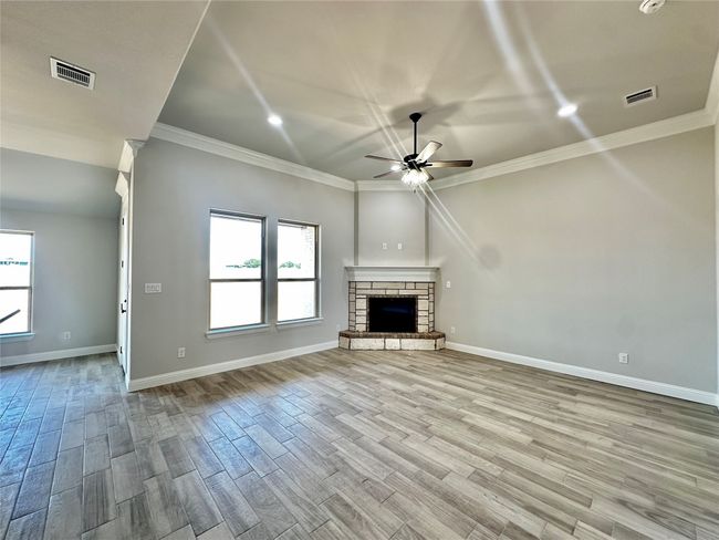 Unfurnished living room featuring a ceiling fan, ornamental molding, wood finished floors, baseboards, and a fireplace | Image 5