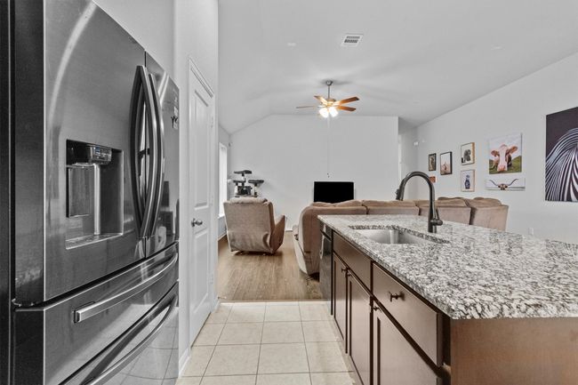 Kitchen featuring stainless steel refrigerator with ice dispenser, a sink, light stone countertops, an island with sink, and dishwashing machine | Image 16