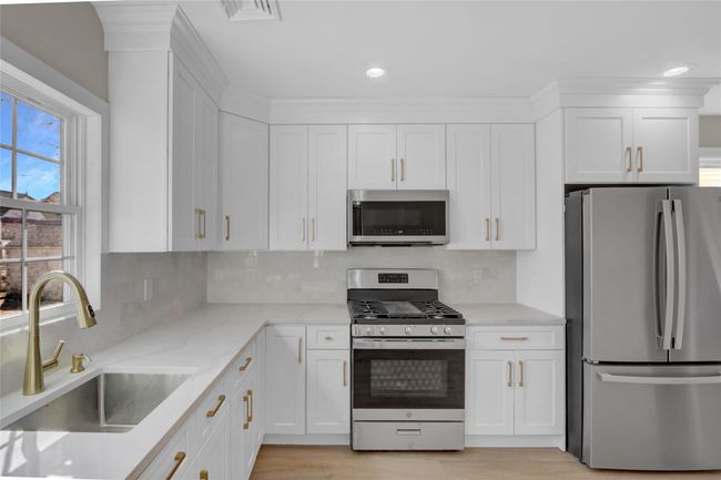 Kitchen with white cabinets, decorative backsplash, stainless steel appliances, and a sink | Image 6