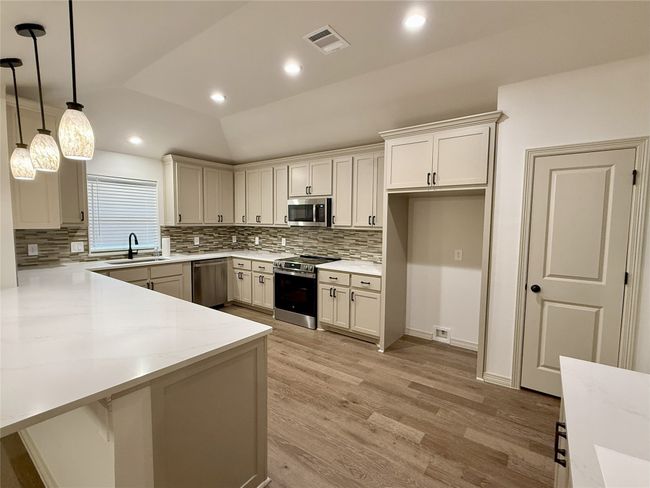 Kitchen featuring appliances with stainless steel finishes, light wood-style flooring, tasteful backsplash, a peninsula, custom cabinets and hanging light fixtures | Image 6