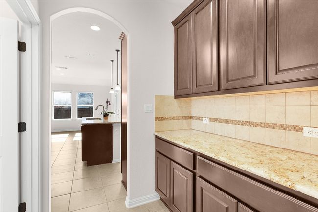Kitchen featuring light stone countertops, light tile patterned flooring, arched walkways, a sink, and decorative backsplash | Image 21