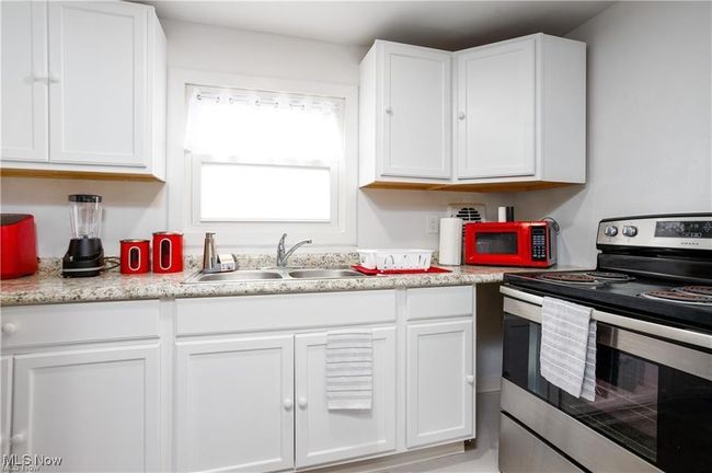 Kitchen with white cabinets, stainless steel electric stove, light countertops, and a sink | Image 8