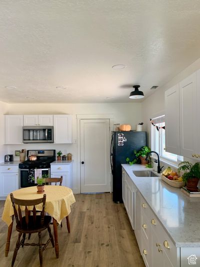 Kitchen featuring light hardwood / wood-style flooring, stainless steel appliances, sink, white cabinets, and a textured ceiling | Image 3