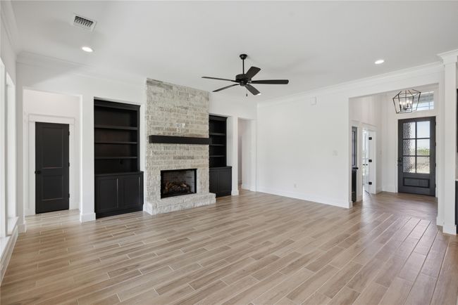 Unfurnished living room featuring crown molding, ceiling fan with notable chandelier, a fireplace, and light hardwood / wood-style flooring | Image 9