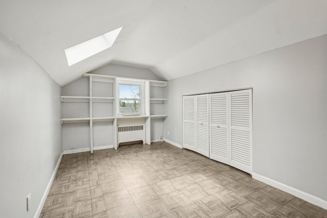 Unfurnished bedroom with radiator heating unit, baseboards, and lofted ceiling with skylight | Image 15