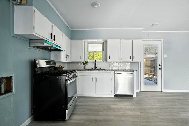 Kitchen featuring appliances with stainless steel finishes, under cabinet range hood, ornamental molding, backsplash, and white cabinetry | Image 8