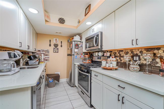 Kitchen with appliances with stainless steel finishes, white cabinets, decorative backsplash, and light stone counters | Image 8
