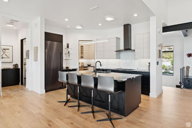 Kitchen with wall chimney range hood, high end refrigerator, modern cabinets, a breakfast bar area, and a kitchen island with sink | Image 16