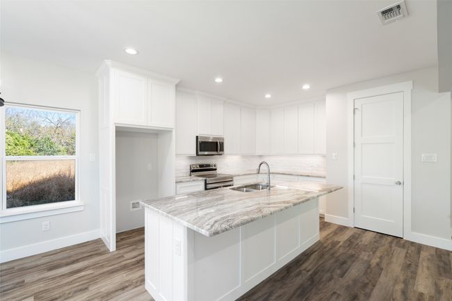 Kitchen with sink, light stone counters, a center island with sink, white cabinets, and appliances with stainless steel finishes | Image 14