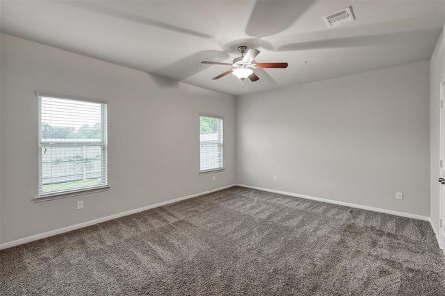 Spacious primary bedroom with neutral color paint and carpet in the back of a house. | Image 14