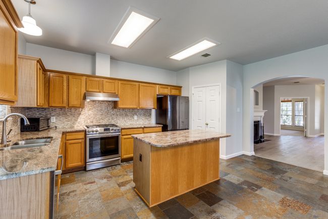 Kitchen featuring appliances with stainless steel finishes, under cabinet range hood, arched walkways, a kitchen island, and decorative backsplash | Image 12