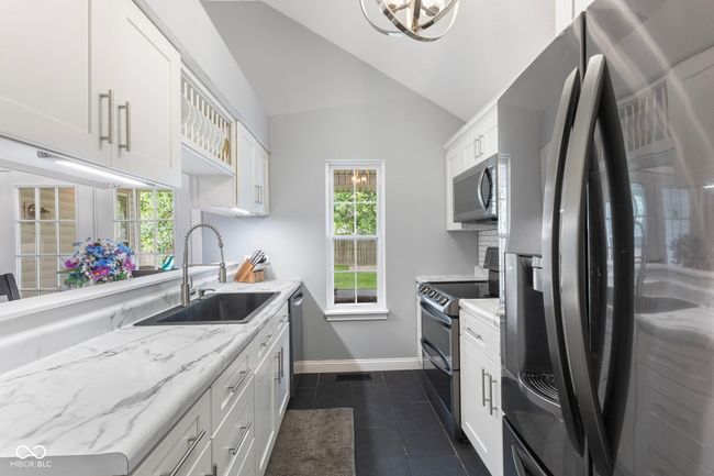 kitchen featuring stainless steel appliances, white cabinetry, lofted ceiling, dark tile patterned floors, and healthy amount of natural light | Image 9