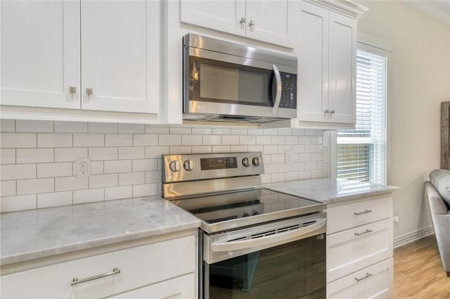 Kitchen featuring stainless steel appliances, decorative backsplash, light stone countertops, white cabinets, and light wood finished floors | Image 10